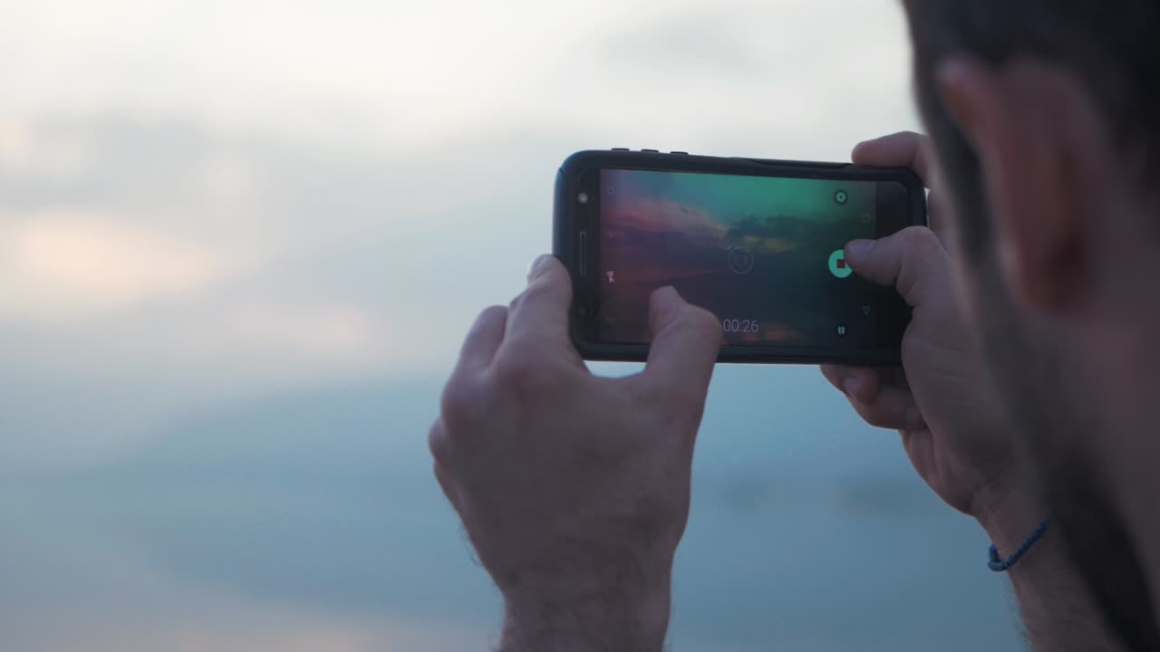 Homem filmando o pôr do sol na hora dourada com o celular - CLIPE LONGO em câmera lenta.