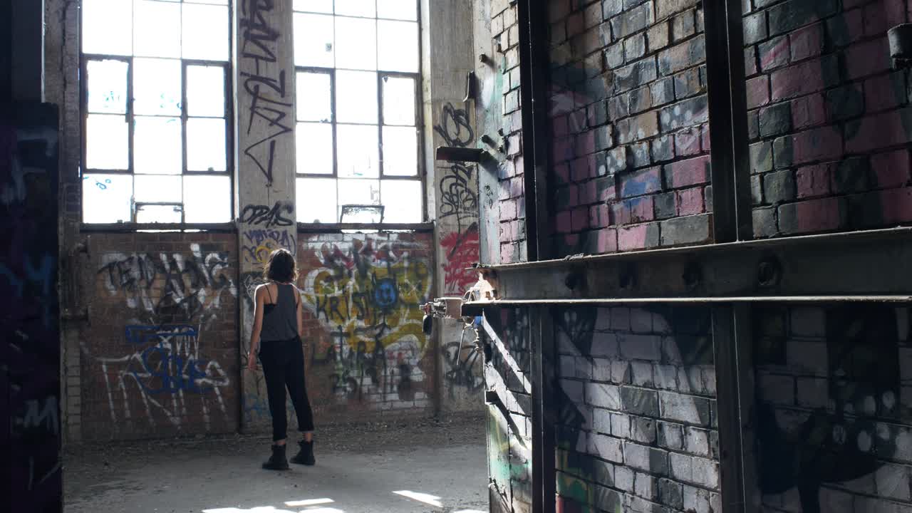 Petite Girl Staring At The Big Windows In A Rundown Warehouse Full Of Graffiti - medium shot