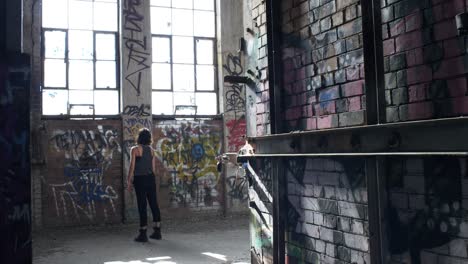 petite girl staring at the big windows in a rundown warehouse full of graffiti - medium shot