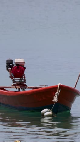 un barco de cola larga roja flota suavemente en aguas tranquilas en phuket, tailandia, bajo la suave luz del día, mostrando un paisaje marítimo sereno