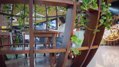 young woman seated in wooden decorative sit-out, holding phone, decorative glowing cat light reflected on tiles in trendy space with vibrant atmosphere