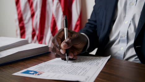 person's hand writing on a ballot or official document with american flag background
