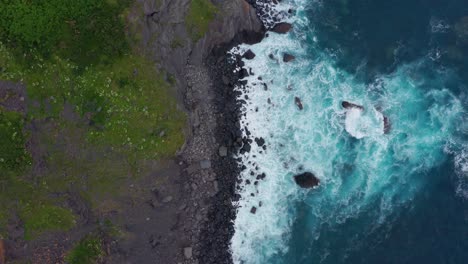 Mossy-cliffs-near-foamy-ocean-in-daylight