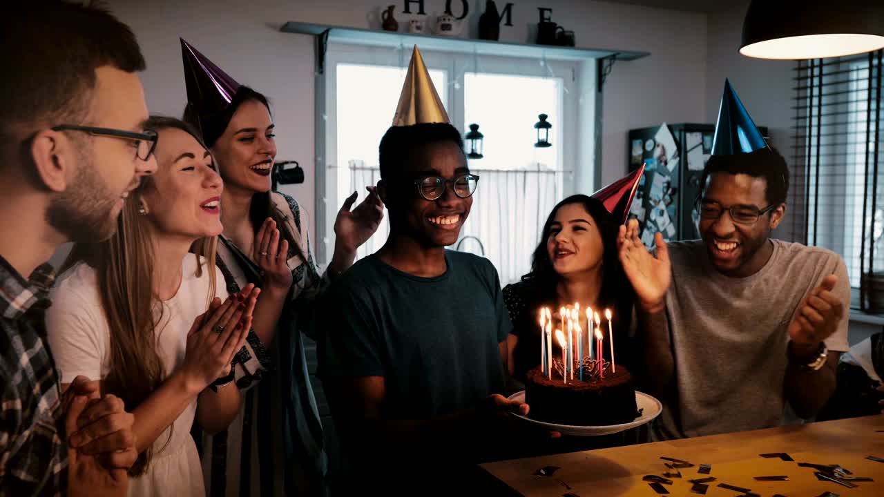 feliz hombre afroamericano sosteniendo pastel de cumpleaños, bailando y celebrando en una fiesta multiétnica con amigos en cámara lenta