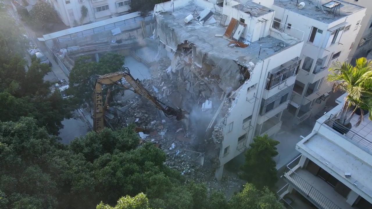 Ampia ripresa aerea in avvicinamento e inclinazione verso il basso attraverso nuvole di polvere in un cantiere di demolizione all'interno di un quartiere urbano consolidato, con drone.