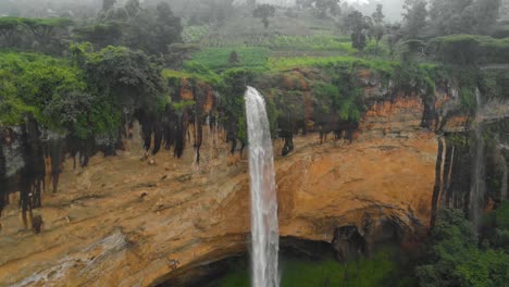 aerial shot orbiting around sipi falls in rural uganda as it plunges off the edge of a cliff into a deep valley