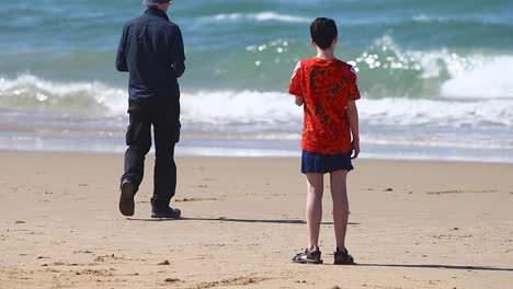 Menschen-Am-Strand-In-Der-Nähe-Der-Tosenden-Wellen-An-Der-Küste,-Aufgenommen-Bei-Sonnenschein,-Freizeit--Und-Freizeitaktivitätenkonzept