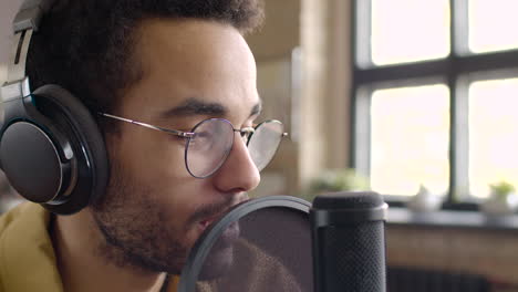 vista de cerca del hombre grabando un podcast usando anteojos y auriculares y hablando en un micrófono 1