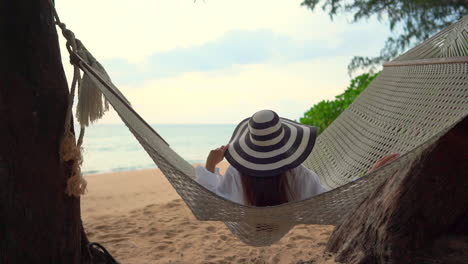 a woman with her back to the camera slowly rocks in a large woven hammock