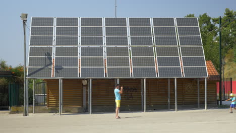 Padre-Toma-Una-Fotografía-De-Su-Hijo-Corriendo-A-Lo-Largo-De-Una-Casa-Con-Paneles-Solares-En-La-Azotea-El-Pireo,-Grecia