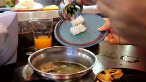 mujer lanza calamar en un caldo hirviendo en un buffet
