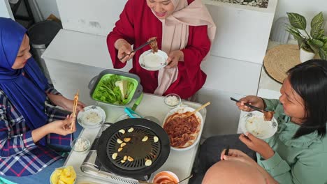 top view of happy asian muslim family eating korean bbq with chopsticks