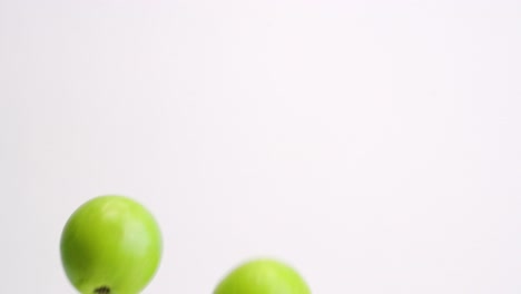 bright green fresh fruit apples raining down on white backdrop and bouncing back up into frame in slow motion