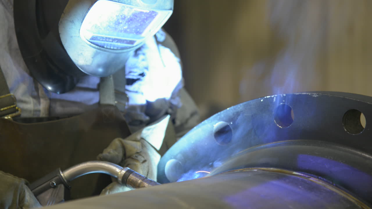 Close up footage of a technician welding a large steel pipe in an industrial machine shop