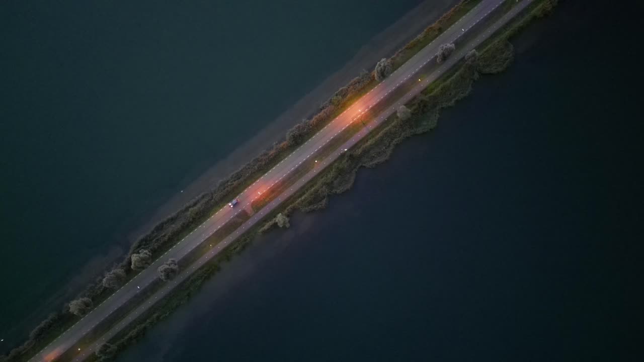 потрясающий воздушный снимок захватывает одинокую дорогу, пересекающую спокойное озеро, с успокаивающими голубыми водами с обеих сторон