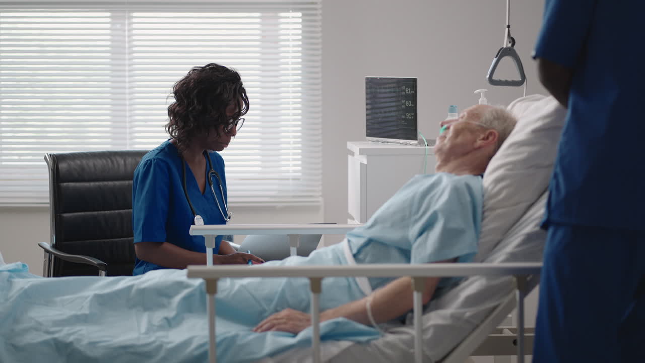 Caring african ethnic medical team at the bedside of an elderly male patient. Caring health care providers monitor vital signs of an elderly male hospital patient