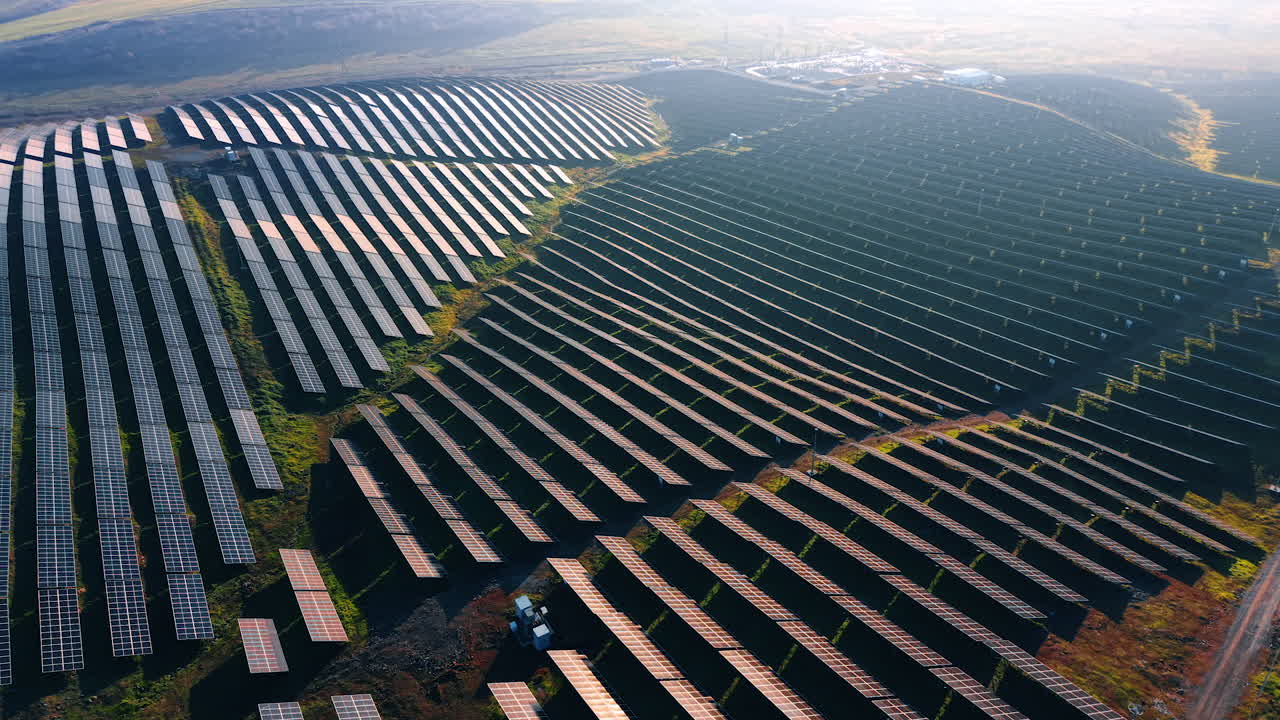 Solpaneler er installeret i pæne rækker på en bjergside. Det er sidst på eftermiddagen, og sollyset fremhæver den vedvarende energikilde. Fjerne strukturer er synlige.