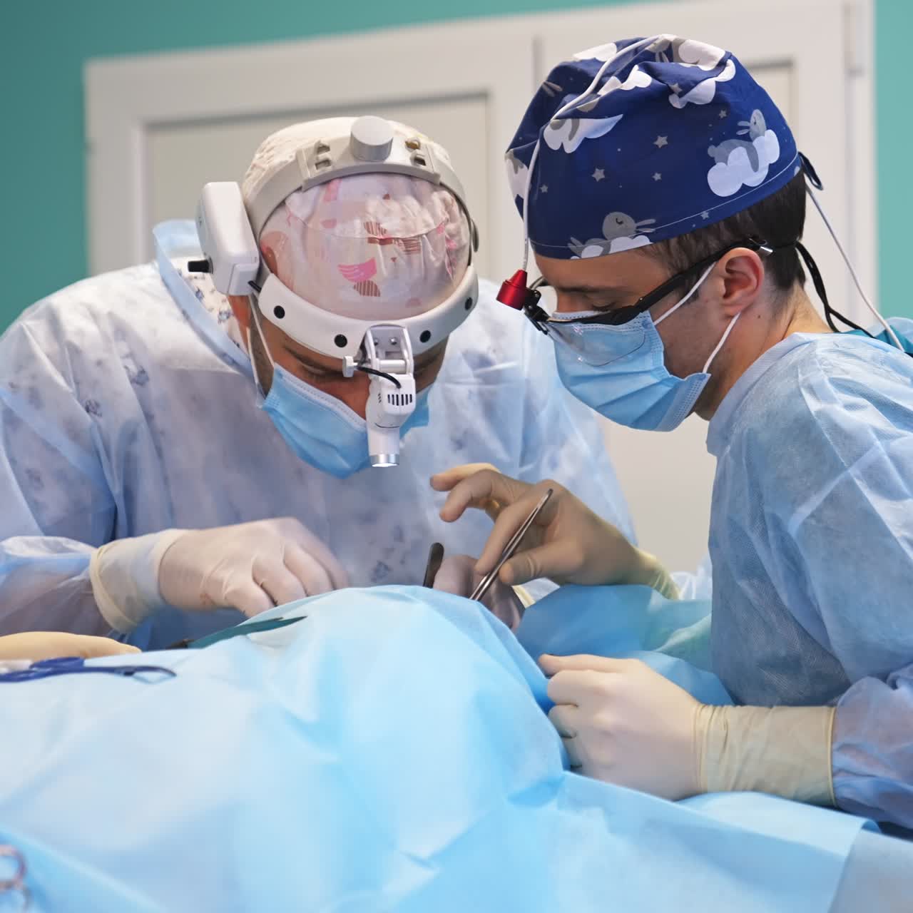 Co working surgeons bent over the patient. Female anesthetist stands at backdrop in the operational room