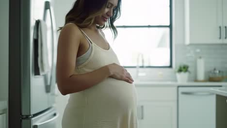 pregnant woman touching her belly in a kitchen