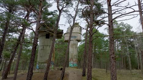 Establishing-aerial-view-of-old-Soviet-military-concrete-observation-watchtower,-pine-tree-forest,-Liepaja-,-military-heritage,-Nordic-woodland,-wide-drone-shot-moving-forward-low