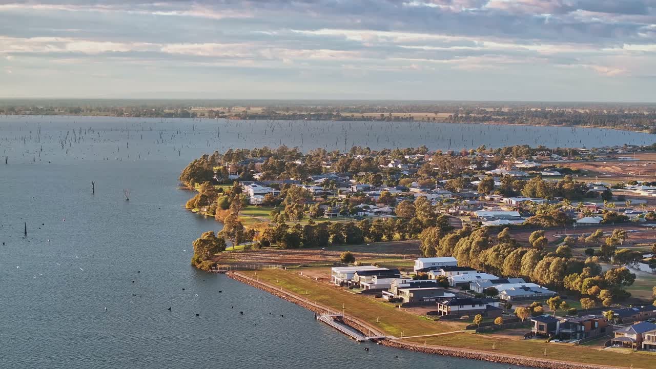 Clustered houses line the edge of a curved peninsula extending into Lake Mulwala at sunset