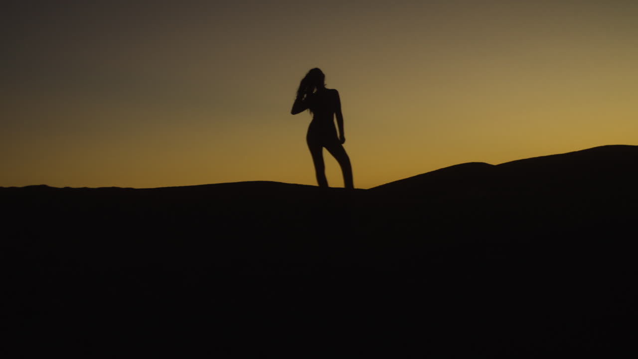 silueta de una mujer bailando en la cima de una duna de arena en el desierto durante una impresionante puesta de sol