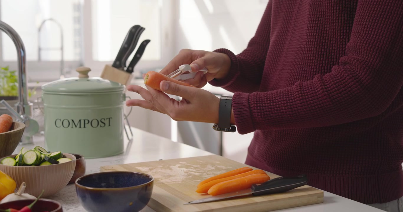 Reaching for peeler, home cook is peeling carrots, scooping shavings into compost for disposal