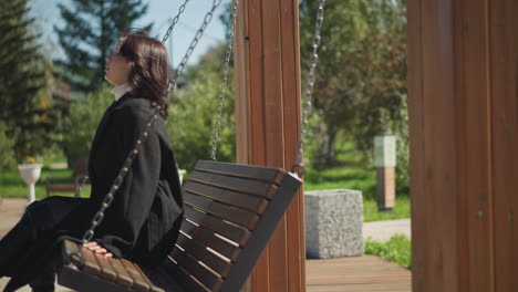 serene moment captured as a woman enjoys the gentle swing motion in a sunlit park, her hair softly moving with the breeze, surrounded by lush greenery