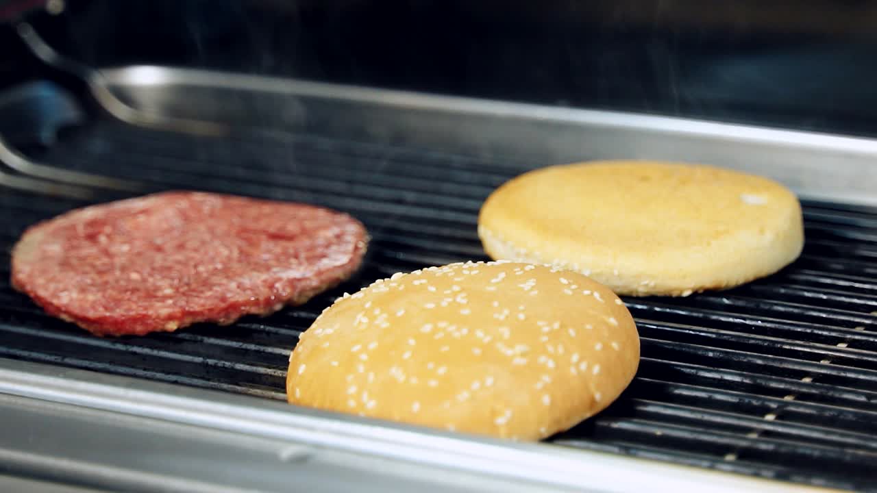 Frying ingredients for hamburger. Cooking buns and cutlet on hot grill. Fast food preparation concept. Close-up