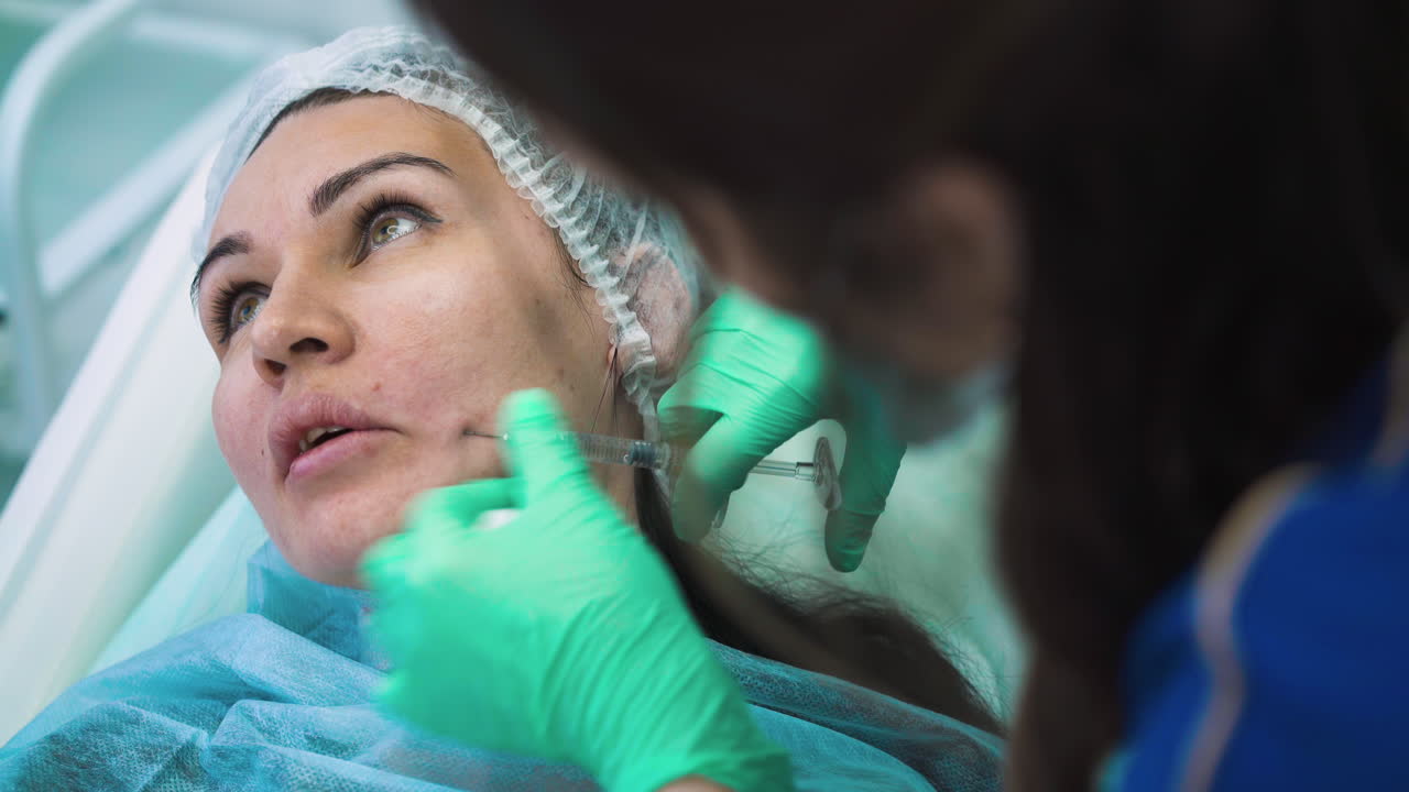 mujer inserta la aguja debajo de la piel del cliente para la inyección de relleno