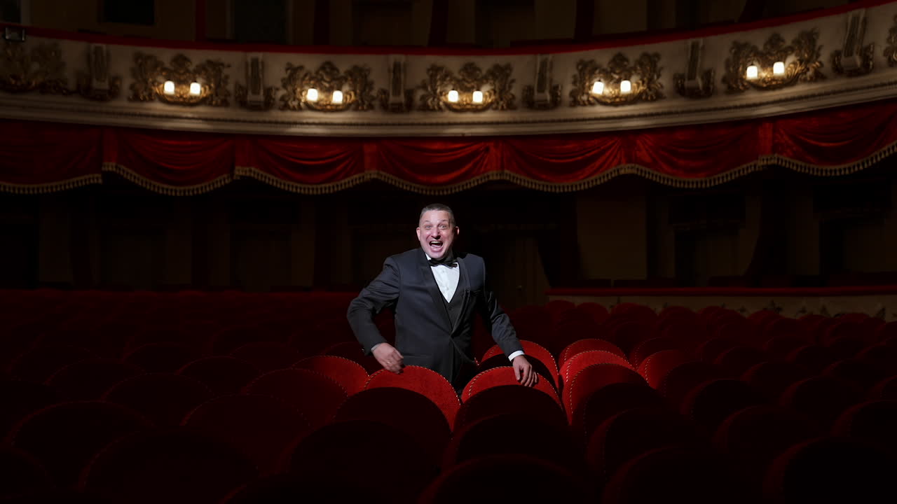 Disappointed actor in empty theatrical hall. Man in costume standing among vacant red seats and calling someone. No audience in opera house. Pandemic in the world.