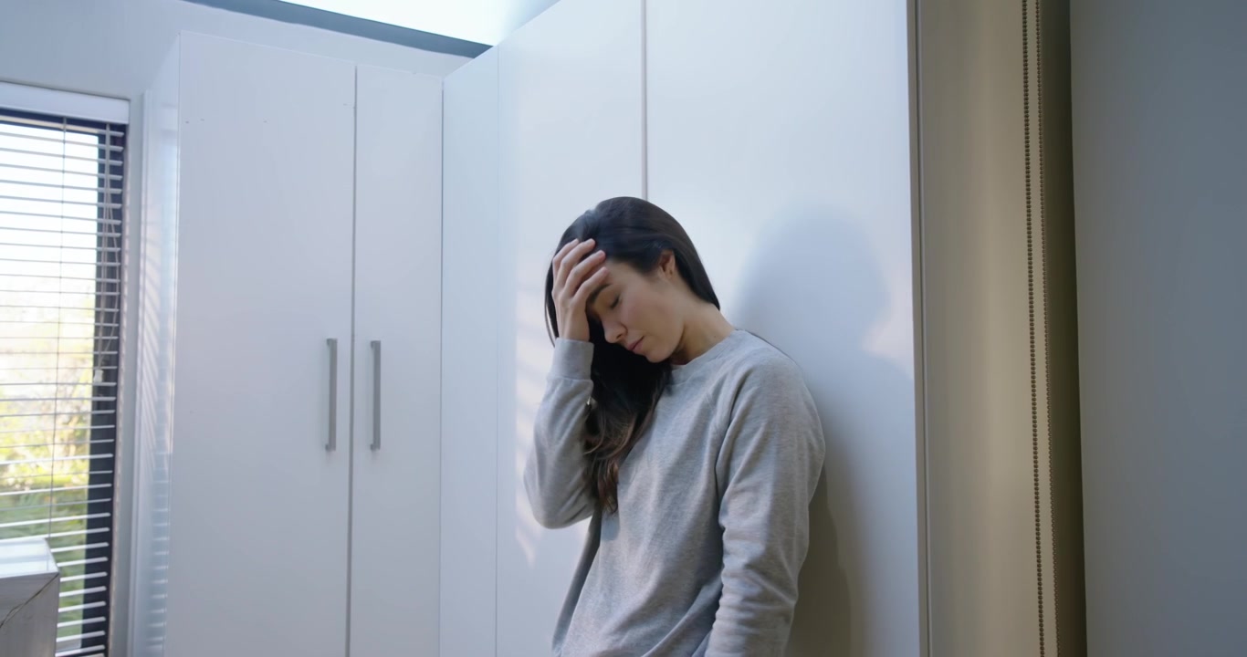 女子穿著灰色睡衣在睡房裡靠著衣櫃，手持紅色手機輕觸並滑動訊息。