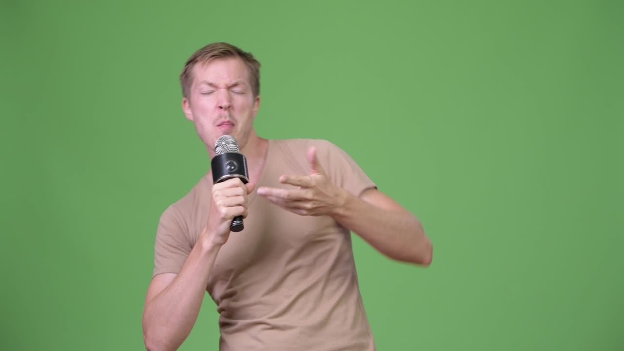 Young handsome Scandinavian man singing against green background