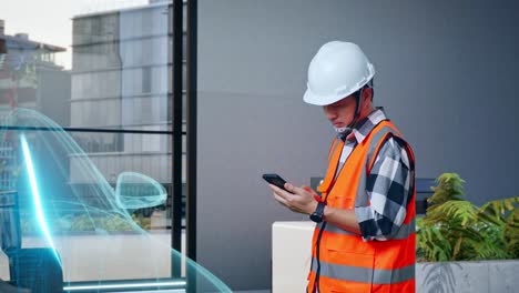 vista lateral de un ingeniero masculino asiático con casco de seguridad usando un teléfono inteligente mientras está de pie con el concepto de vehículo eléctrico, instalación industrial de alta tecnología