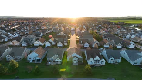 Suburban-neighborhood-at-sunset,-with-rows-of-similar-houses,-green-lawns,-and-a-street-leading-directly-into-the-glowing-sun-on-the-horizon