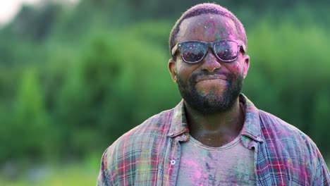 retrato del joven apuesto y alegre sonriendo a la cámara mientras está de pie al aire libre y sonriendo con pintura en polvo en el festival holi