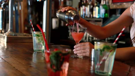 barmaid pouring cocktail in glass at bar counter