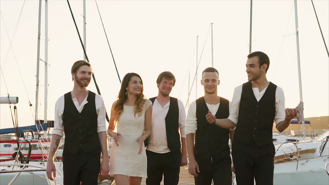 Group of friends walking on a dock by boats at sunset