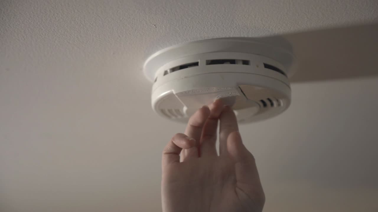 Turning On With One Hand The Smoke Detector On The White Ceiling. -medium shot