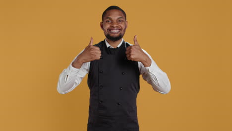 Waiter-smiling-and-showing-a-thumbs-up-symbol-against-yellow-background