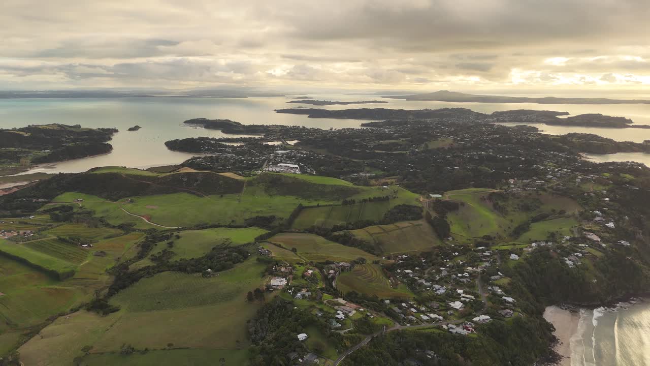 Waiheke Island with green mountains and and houses located on hilltop. Sunrise in New Zealand. Onetangi Beach area and tropical islands in distance. Aerial wide shot.