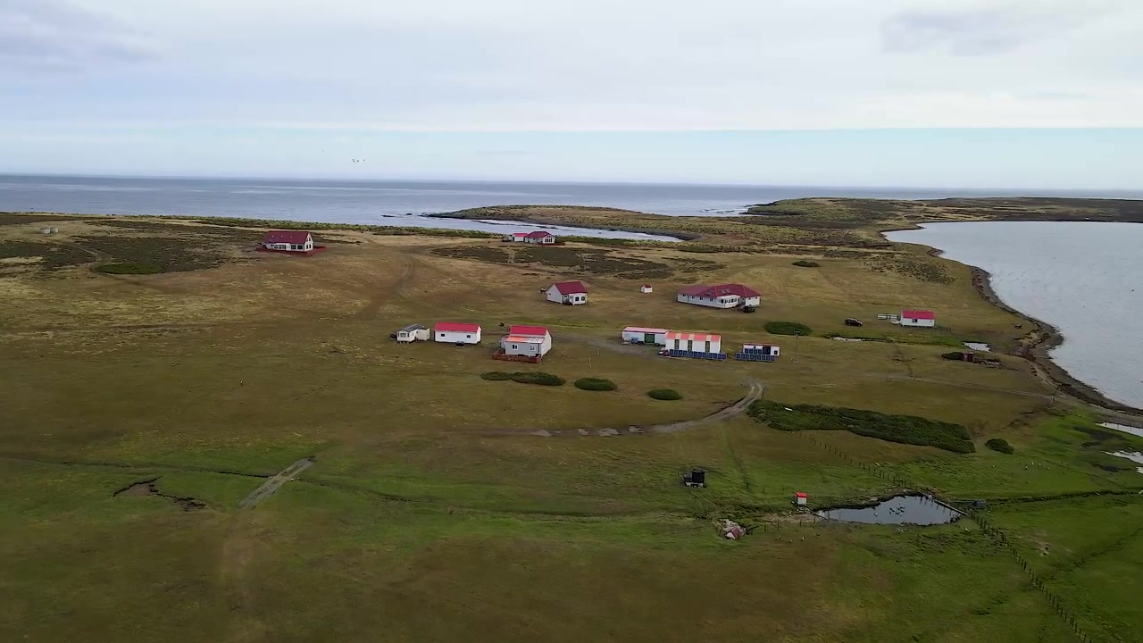 Kameraschwenk über ein abgelegenes Inseldorf enthüllt charmante Häuser und Nebengebäude, eingebettet in eine ruhige Landschaft