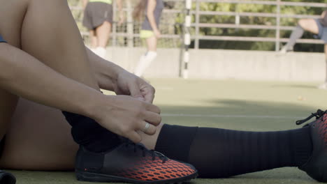 Primer-Plano-De-Una-Jugadora-De-Fútbol-Femenina-Irreconocible-Atándose-Los-Zapatos-Mientras-Se-Sienta-En-El-Campo