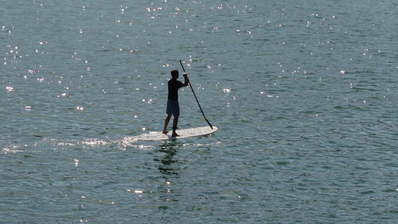 silueta de stand up paddle boarder con sol matutino reflejándose en el agua
