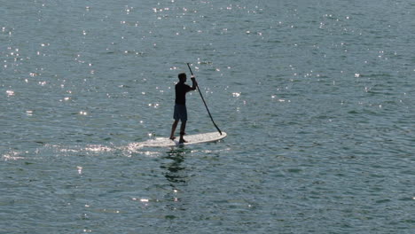 silueta de stand up paddle boarder con sol matutino reflejándose en el agua