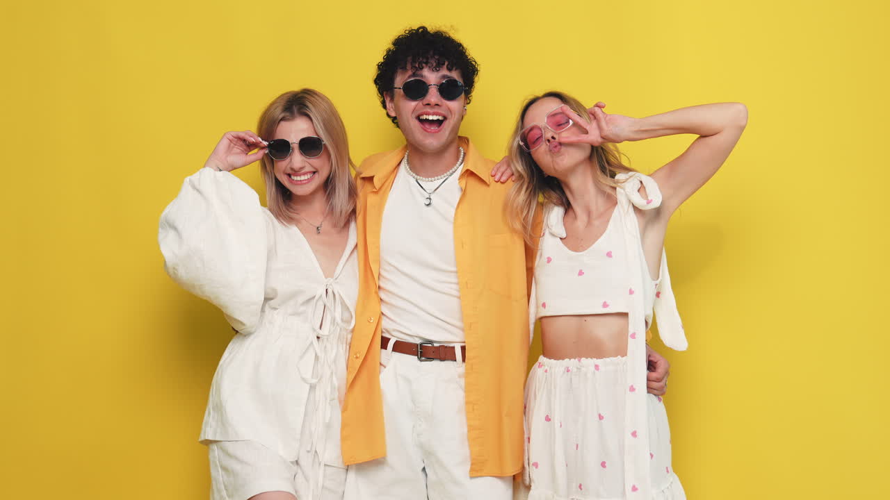 노란색 배경 에 세 친구 가 세련 된 옷 을 입고 포즈 를 취 하고 있다
