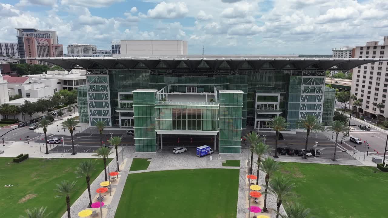 Modern Dr. Phillips Center Building in Orlando City with palm trees and parking cars. Cloudy day in Florida, USA. Aerial approaching shot. Performing arts center in Downtown.