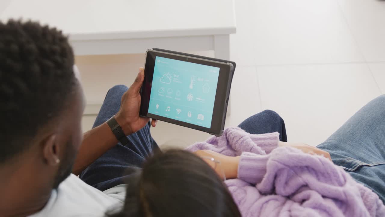 Happy diverse couple lying and using tablet in living room