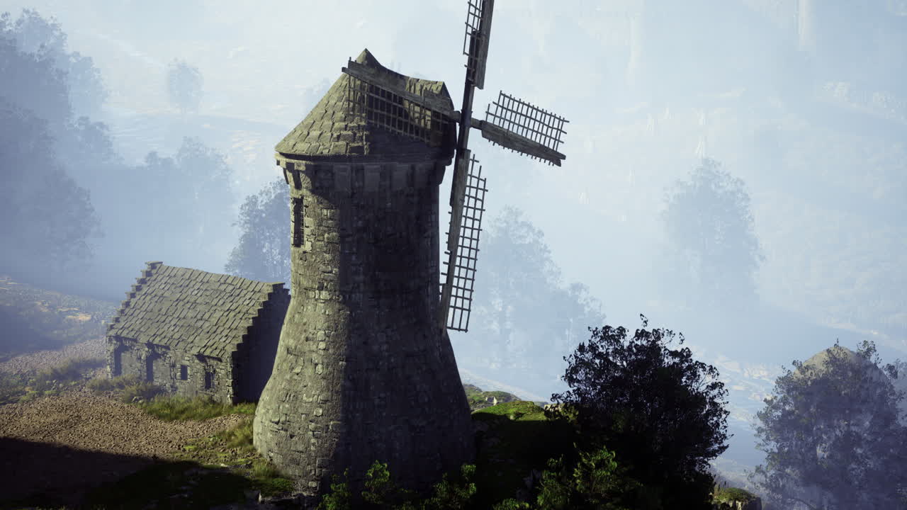 역사적인 풍차는 새벽에 안개가 가득한 시골 풍경 속에서 웅장하게 서 있습니다.