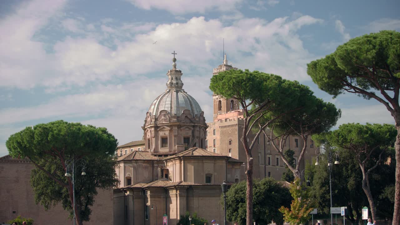 Gereja Nama Tersuci Maria di Roma dengan kubah yang detail dan pohon pinus di sekitarnya di bawah langit cerah, menciptakan pemandangan arsitektur bersejarah klasik di kota Italia.